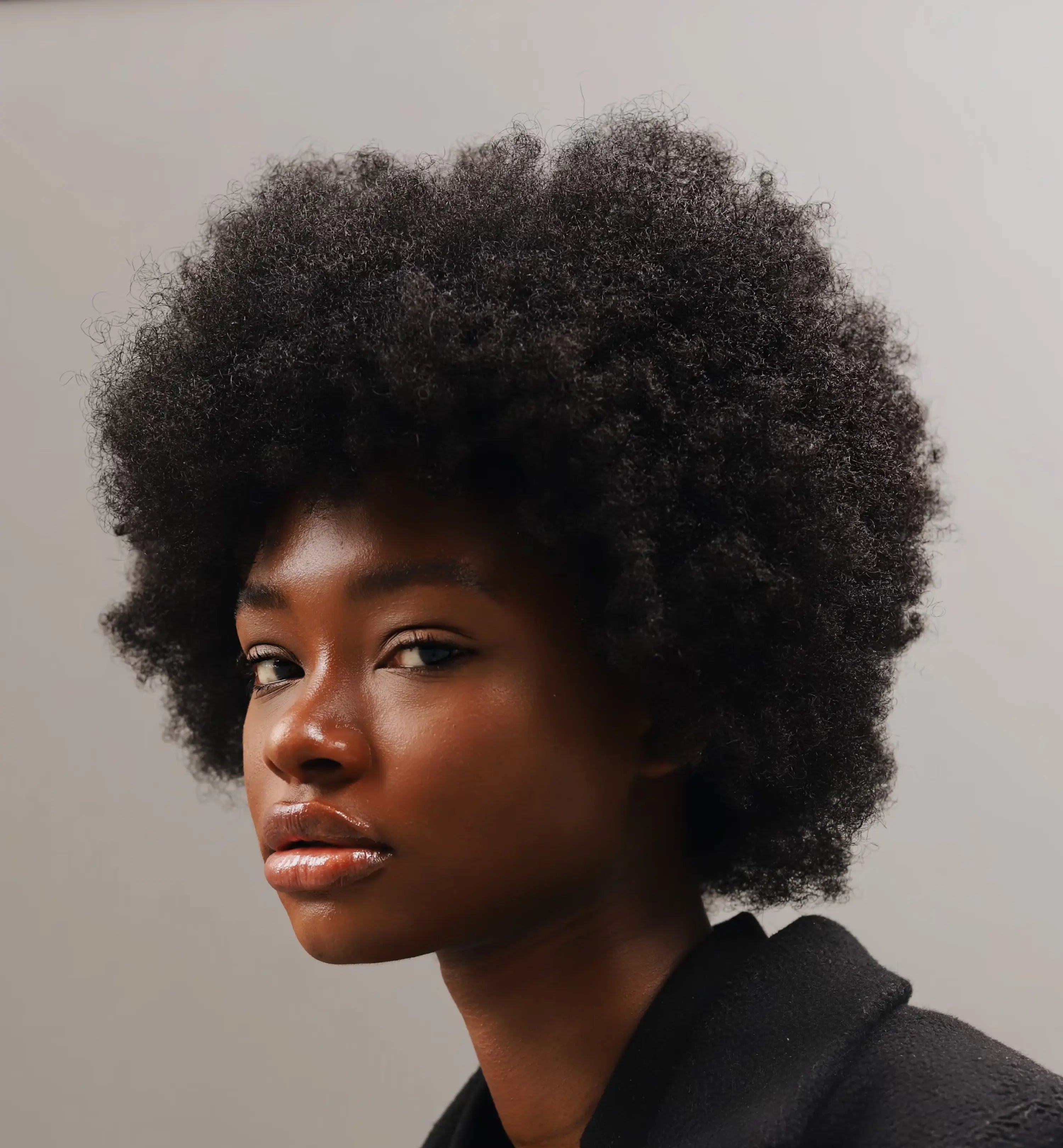 Confident woman with natural afro-textured hair and glowing skin — portrait showcasing healthy hair and minimalist beauty